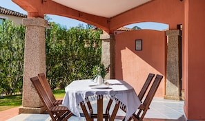 Une terrasse extérieure avec une table ronde, deux chaises en bois, une nappe blanche et un vase rempli de fleurs.