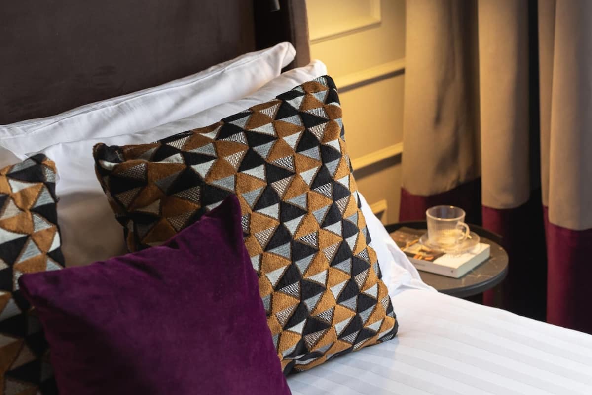 A neatly made bed with patterned pillows, a bedside table with a glass, and a hanging lamp.