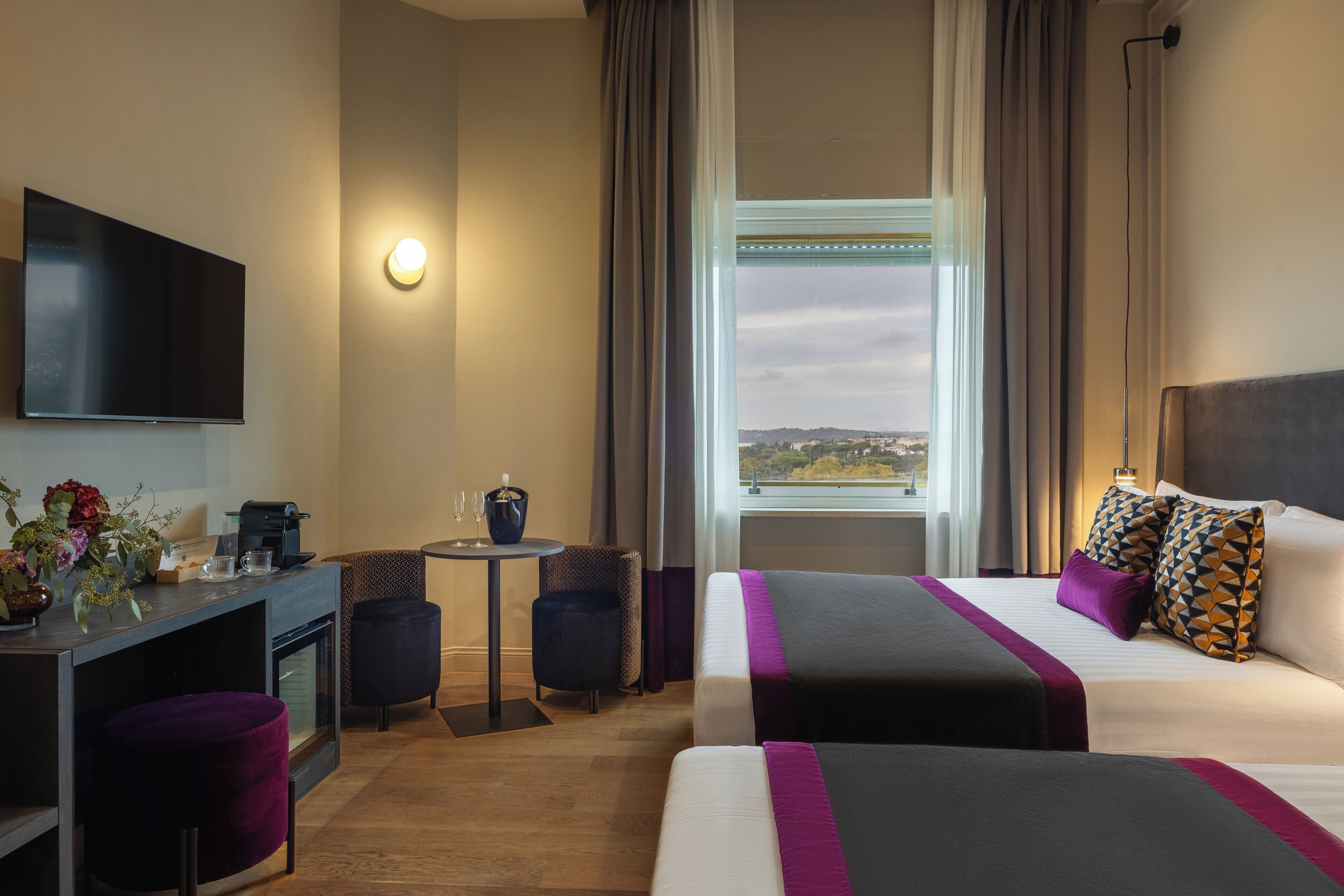 A hotel room with a bed, a desk, a TV, a small table, and a window with a view.