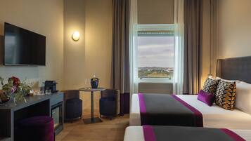 A hotel room with a bed, a desk, a TV, a small table, and a window with a view.