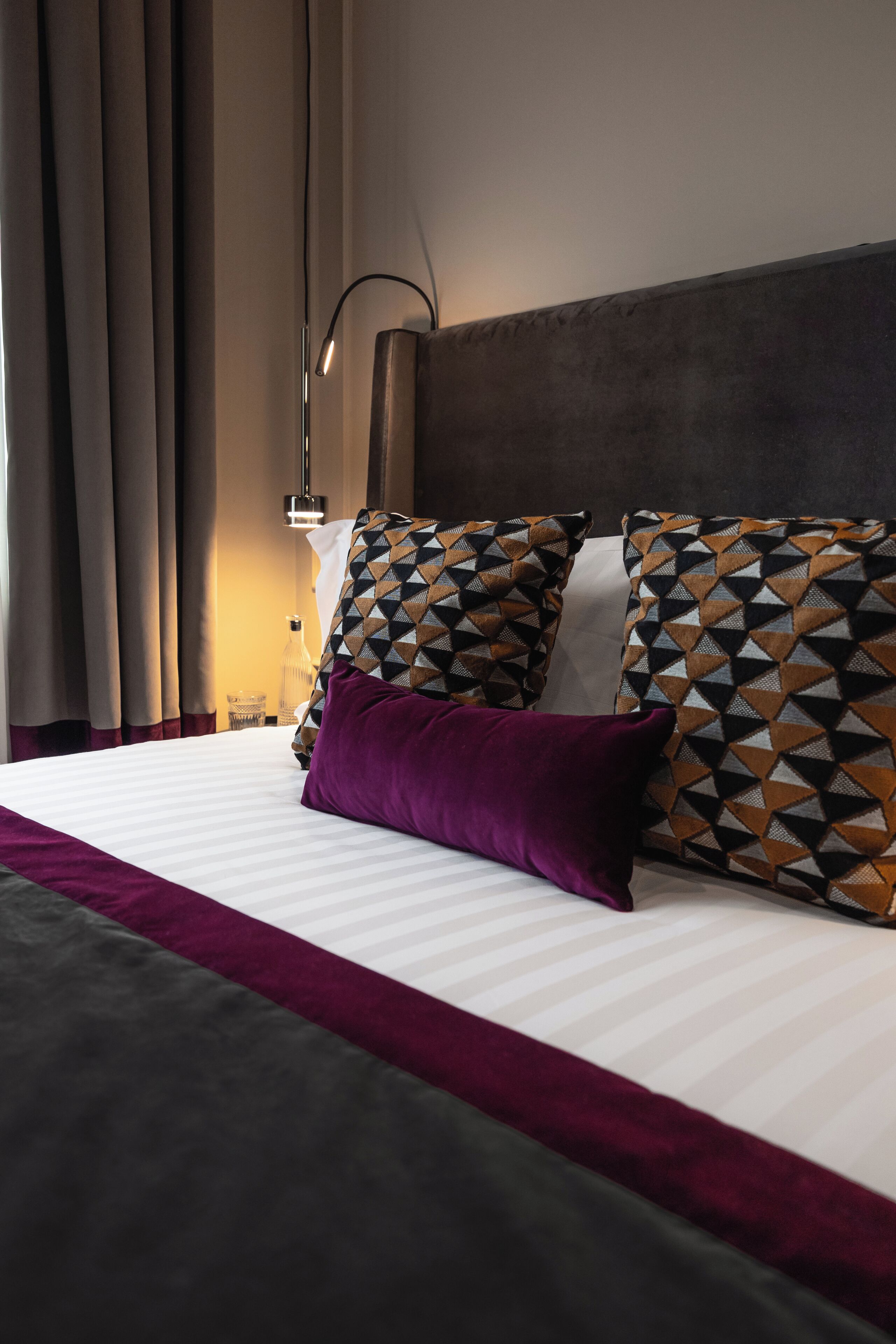 A neatly made bed with patterned pillows, a bedside lamp, and curtains.