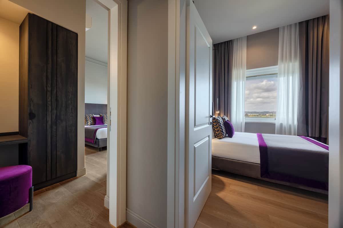 A modern hotel room with a bed, a seating area, and a view of the outdoors.