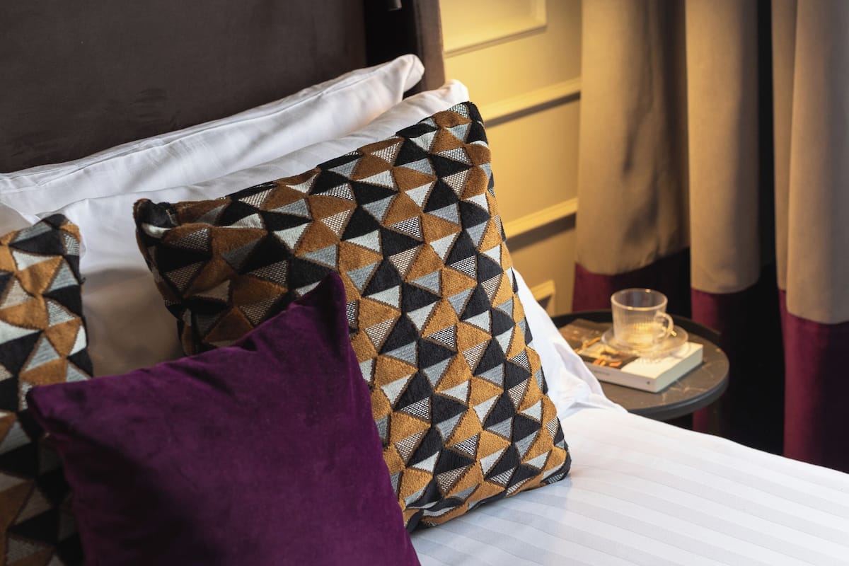A neatly made bed with patterned pillows, a bedside table with a glass, and a lamp.