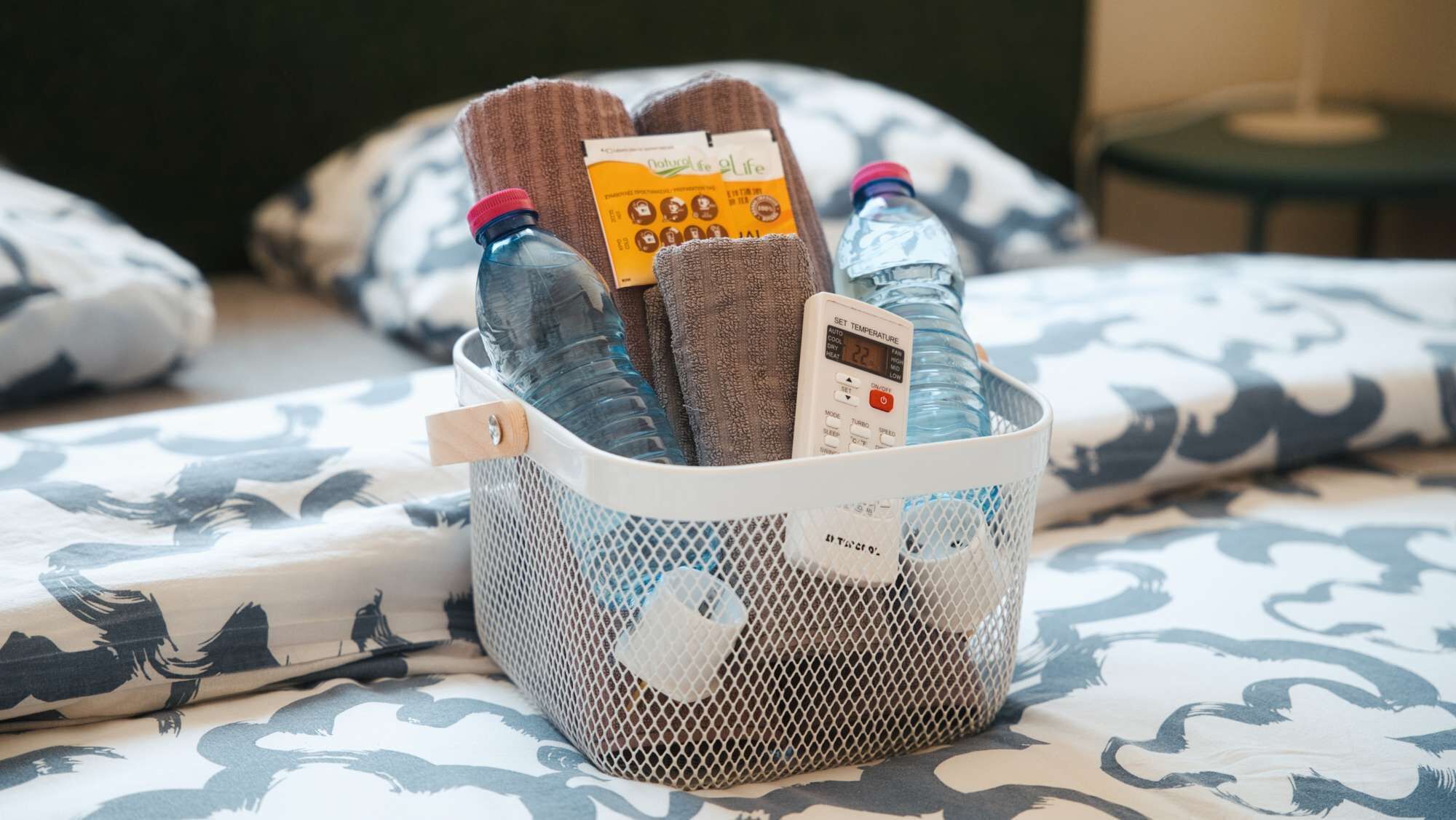 A basket containing bottles and a portable heater on a bed with patterned bedding.