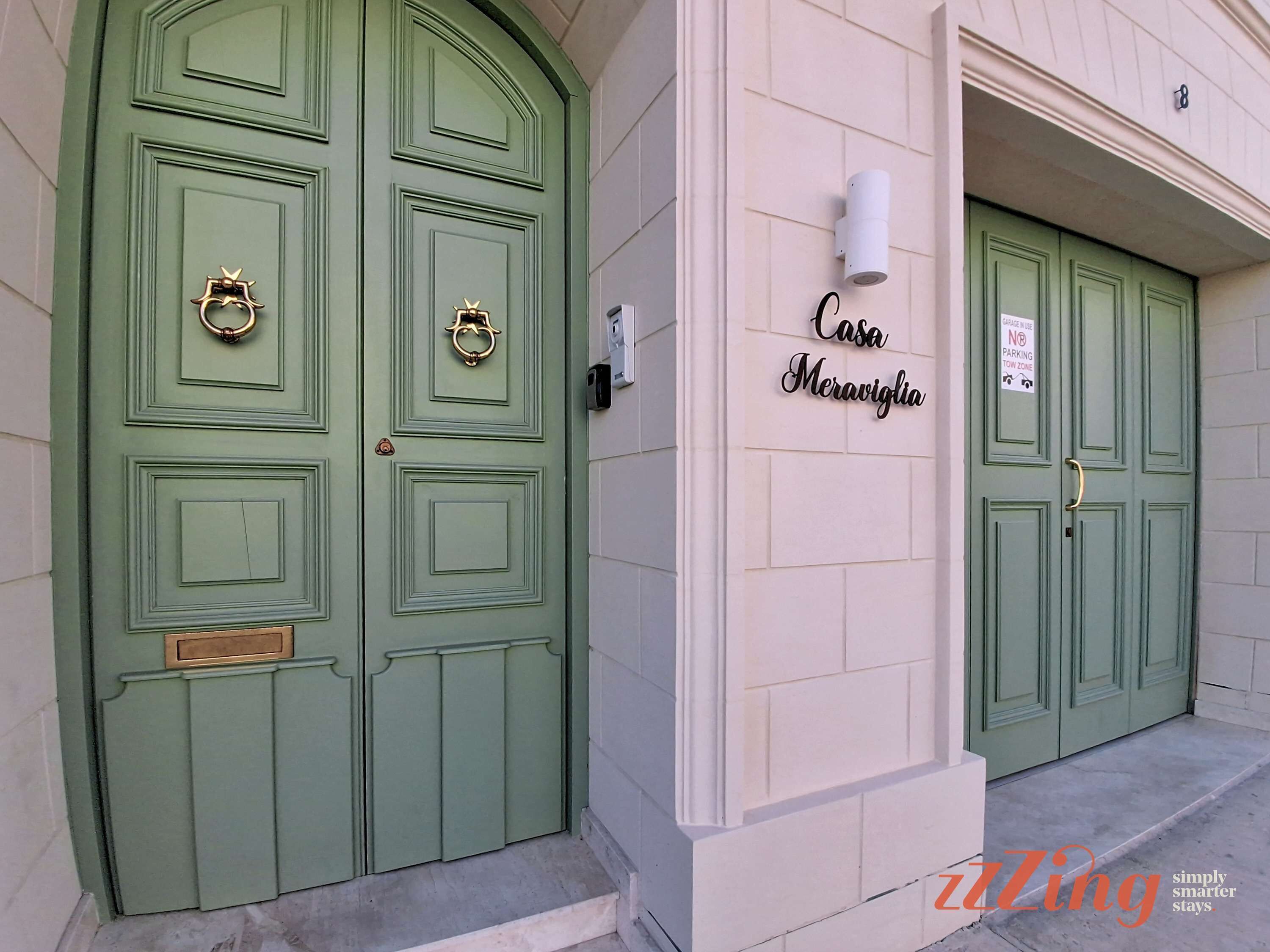 A building with green double doors, a wall-mounted sign reading "Casa Meraviglia", and a "No Parking" sign.