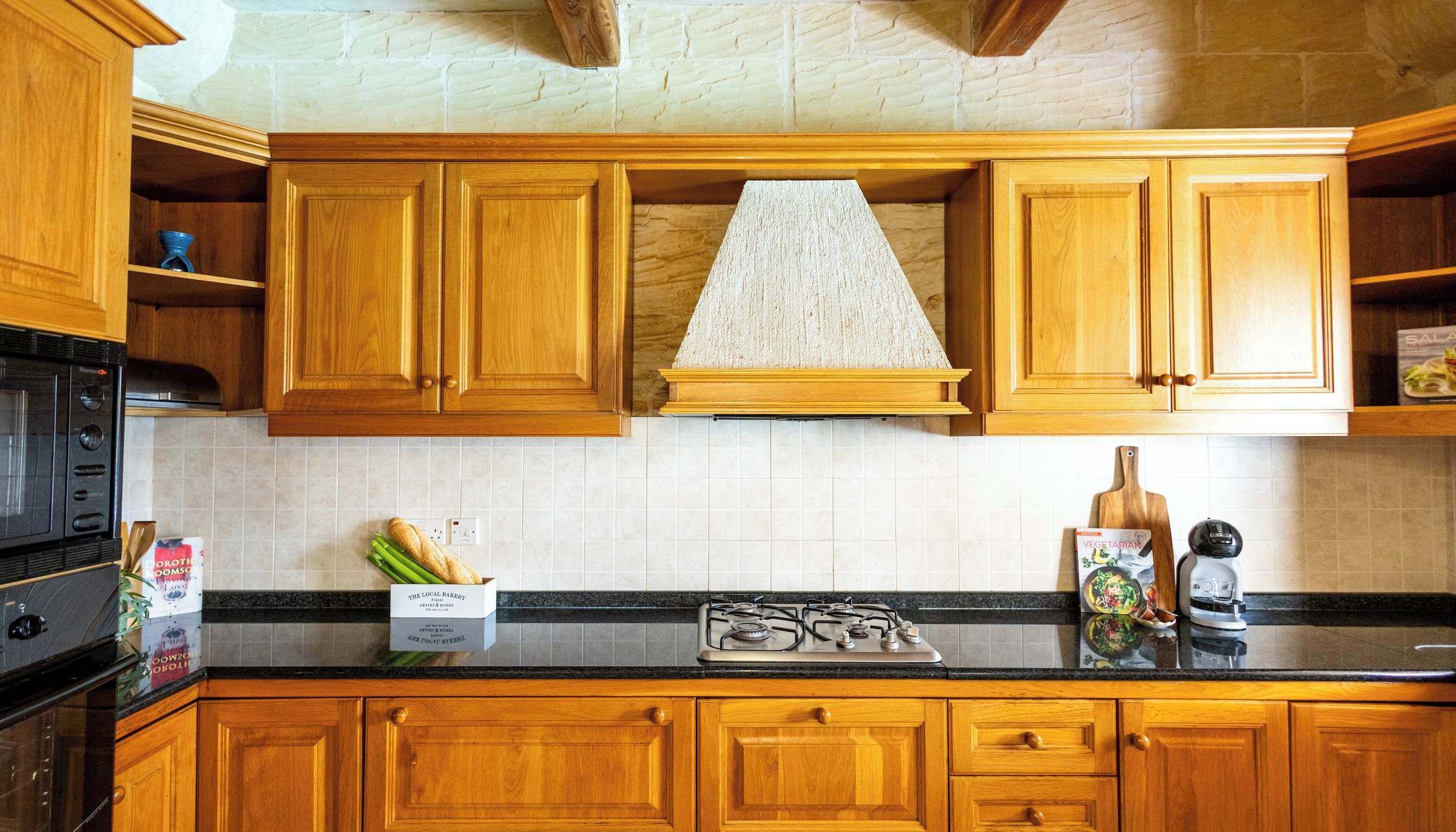 A kitchen with wooden cabinets, a black countertop, a stove, and a box of bread.