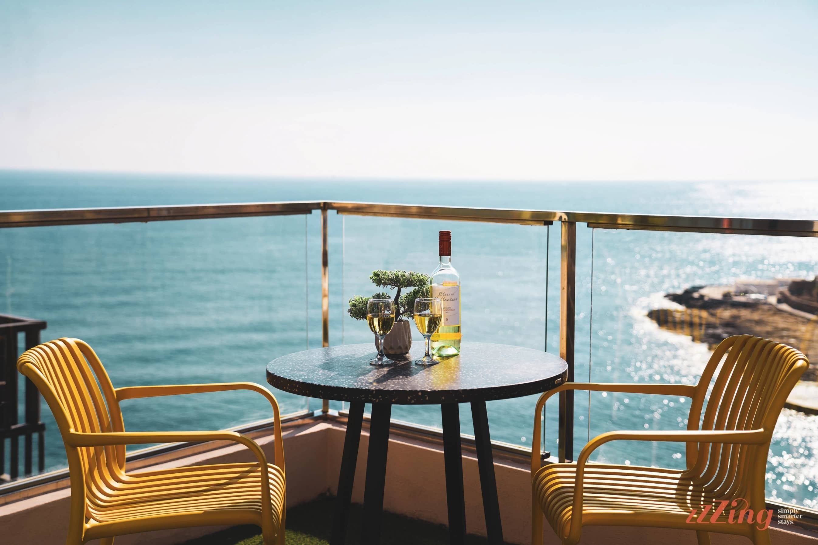 Un balcon avec une table ronde et deux chaises jaunes, offrant une vue sur la côte.