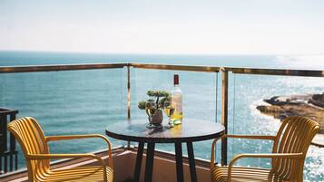 Un balcon avec une table ronde et deux chaises jaunes, offrant une vue sur la côte.