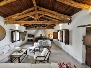 A rustic interior with a high wooden ceiling, white walls, a sofa, chairs, a table with fruit, and a fireplace. - Finca Fiori 1 – Experience Authentic Sardinia in an Exclusive Country Villa (S.Margh.di Pula)