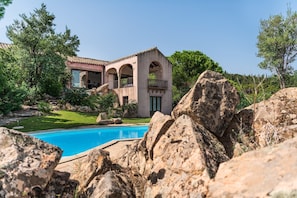 Uma casa com piscina, rodeada por pedras grandes e vegetação.