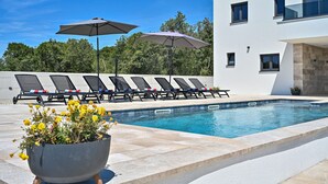 A modern pool area with lounge chairs and umbrellas, surrounded by a white building with large windows. - Villa Donatus Zadarvillas (Policnik)