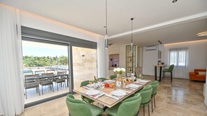 A dining area with a large table set for six, surrounded by green chairs, with a view of a pool and outdoor seating. - Villa Donatus Zadarvillas (Policnik)