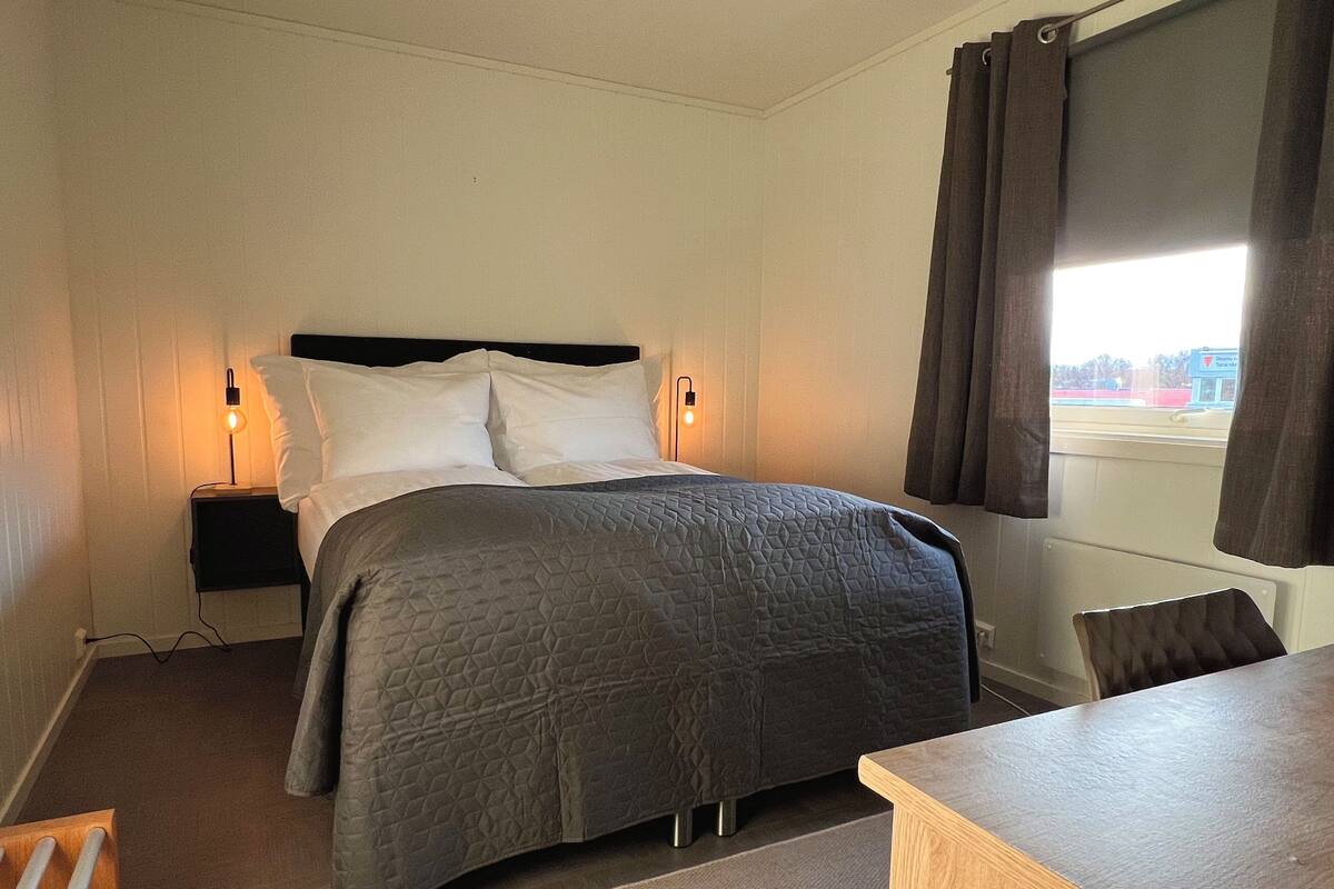 Una habitación de hotel con cama, lámparas de noche, un escritorio y vistas al exterior.