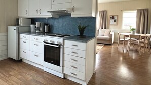 A modern kitchen with white cabinets, a built-in oven, and a microwave. There is a dining area with a table and chairs. - Tanabrew  (Tana)