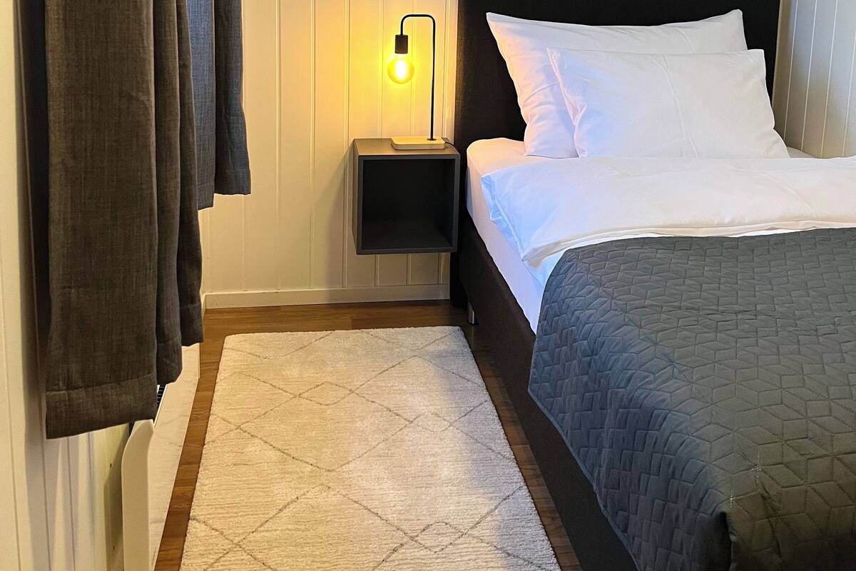 Un dormitorio con una cama, una mesita de noche con lámpara y una ventana con cortinas.