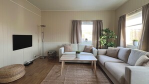 A living room with a sofa, a coffee table, a TV, and a window with curtains. - Tanabrew  (Tana)