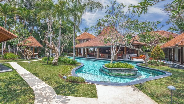 Ein Resort mit einem zentral gelegenen Schwimmbad, mehreren bungalowsartigen Unterkünften mit roten Ziegeldächern und üppiger tropischer Bepflanzung.