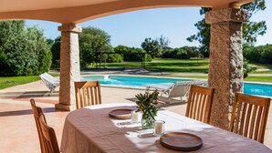 Ein überdachter Essbereich im Freien mit Blick auf einen Pool, Holzstühle und ein Tisch für zwei Personen.