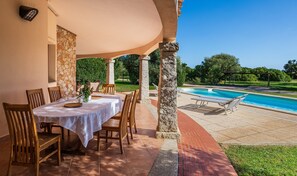 A covered outdoor dining area with a pool view, stone pillars, and a clear blue sky. - Villa Mistral Costa Rei – Beachfront Villa with Private Pool (Costa Rei)