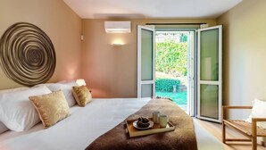 Un dormitorio con cama, almohadas, una bandeja con comida y vasos, un equipo de aire acondicionado y vistas a la vegetación a través de puertas abiertas.