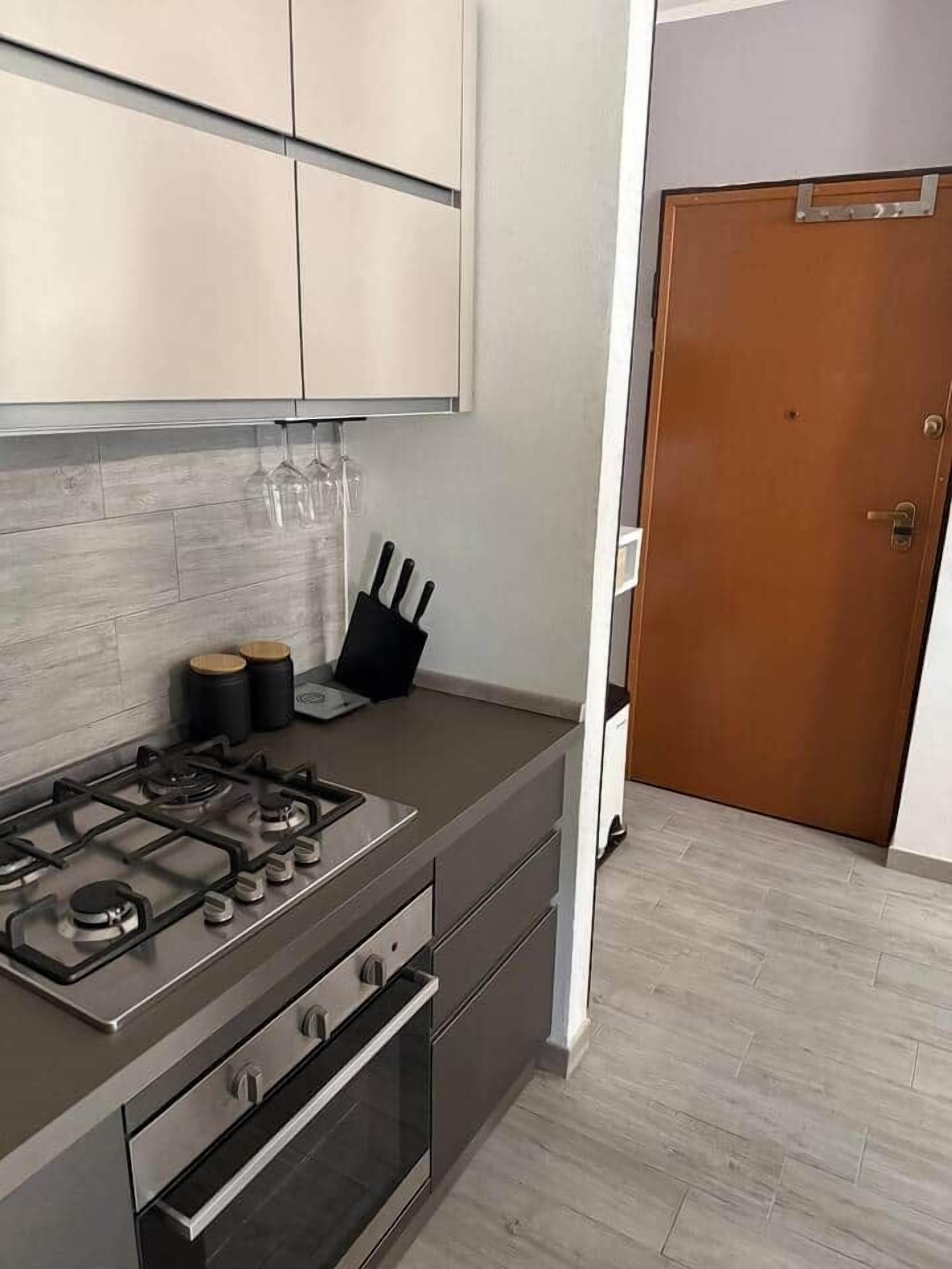 Eine moderne Küche mit Gasherd, Backofen und Edelstahl-Schränken. Im Hintergrund ist eine Holztür zu sehen.