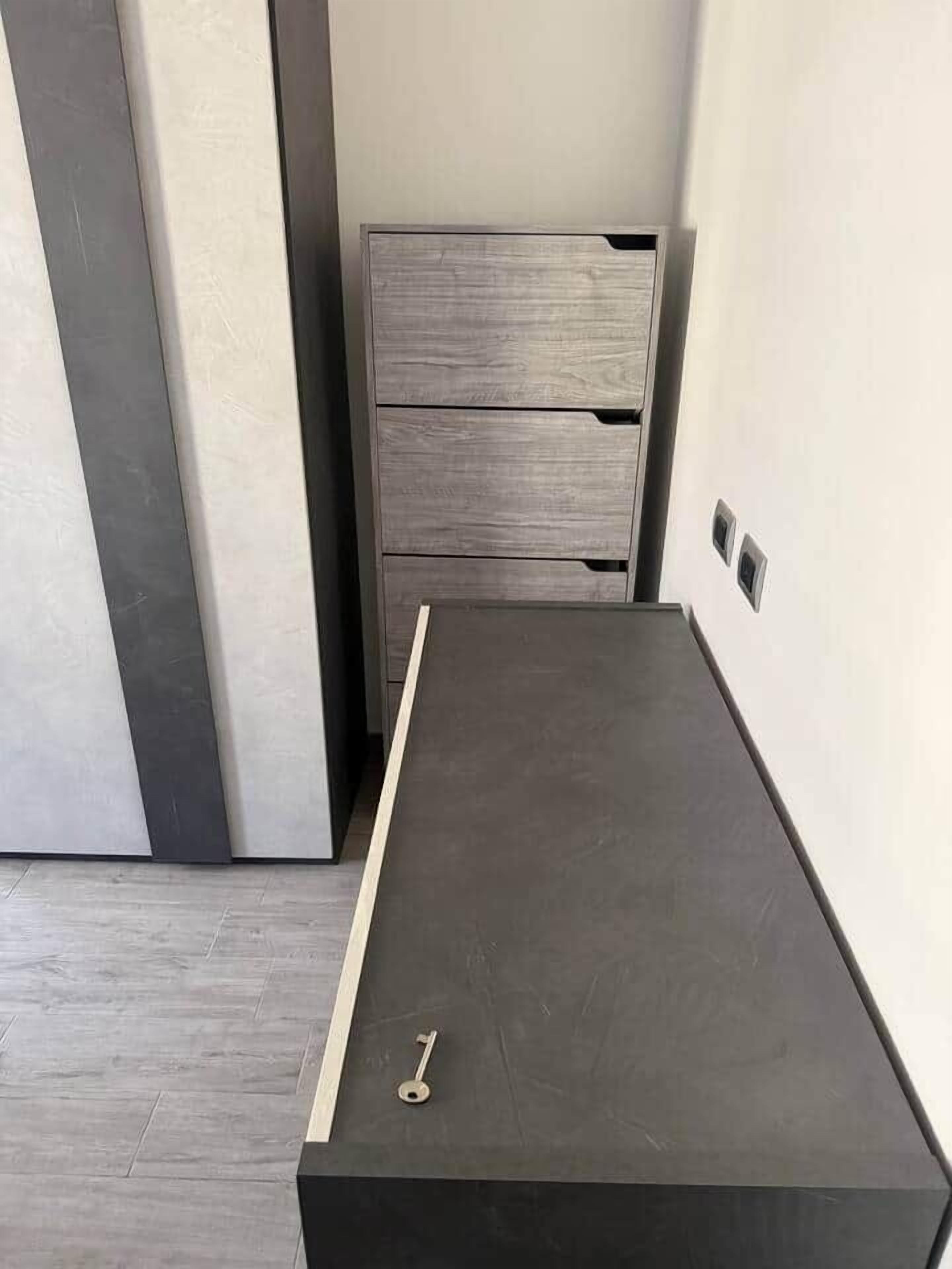 A small, dark-colored desk with a key on it, positioned against a wall with a light switch and a door handle.