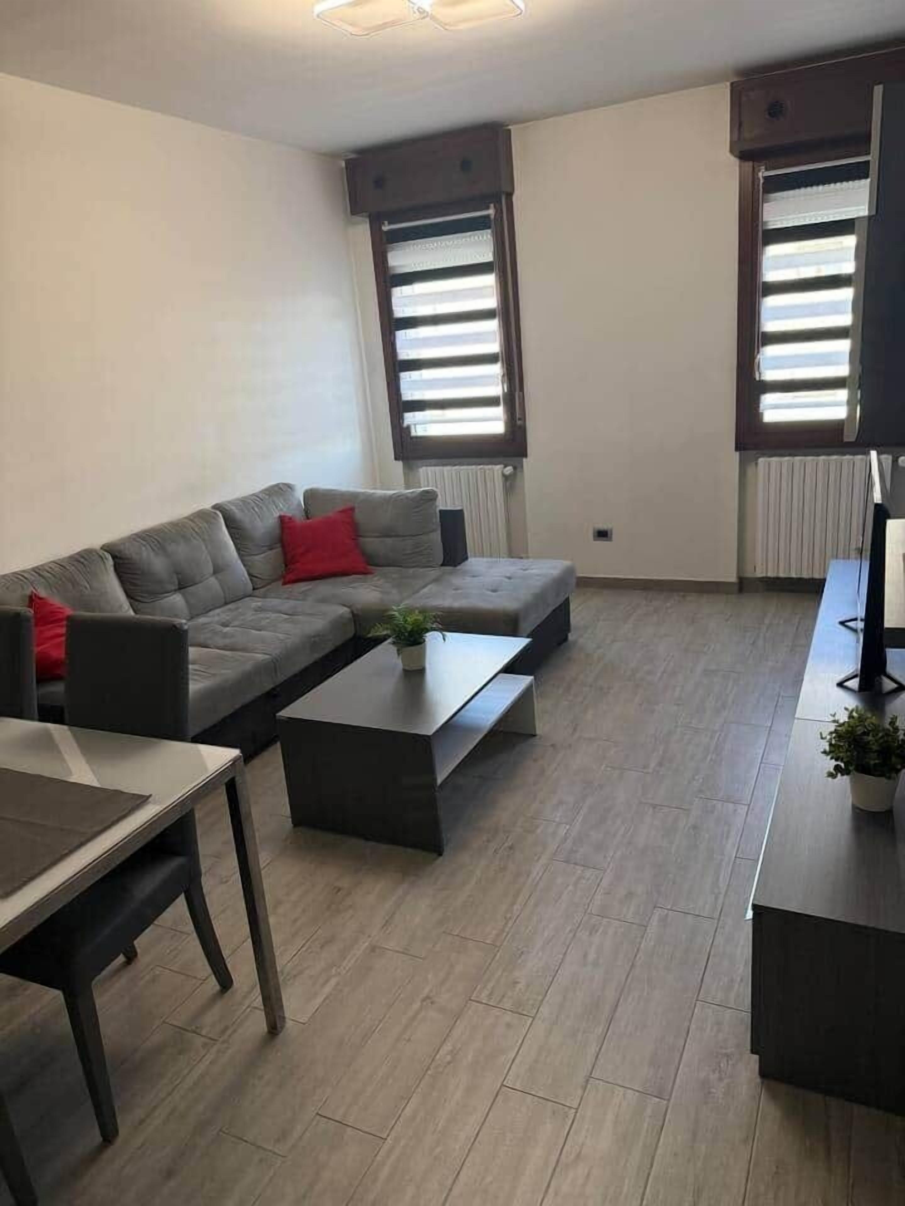 Un salon moderne avec un canapé d’angle gris, une petite table basse, une table à manger et un téléviseur à écran plat.