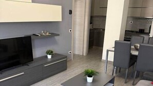 Ein modernes Wohnzimmer mit grauem Sofa, einem Flachbildfernseher, einem Couchtisch und einer kleinen Pflanze.