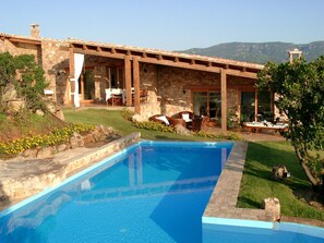 Une piscine avec une terrasse en pierre, un bâtiment en pierre doté d’un patio et une vue sur les montagnes.