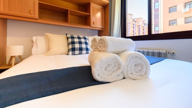 A hotel room with a neatly made bed, a checkered pillow, and a window with a view of buildings. - Stylish accommodation: 2 bedrooms, air conditioning and all mod cons HOR1K1B (Madrid)