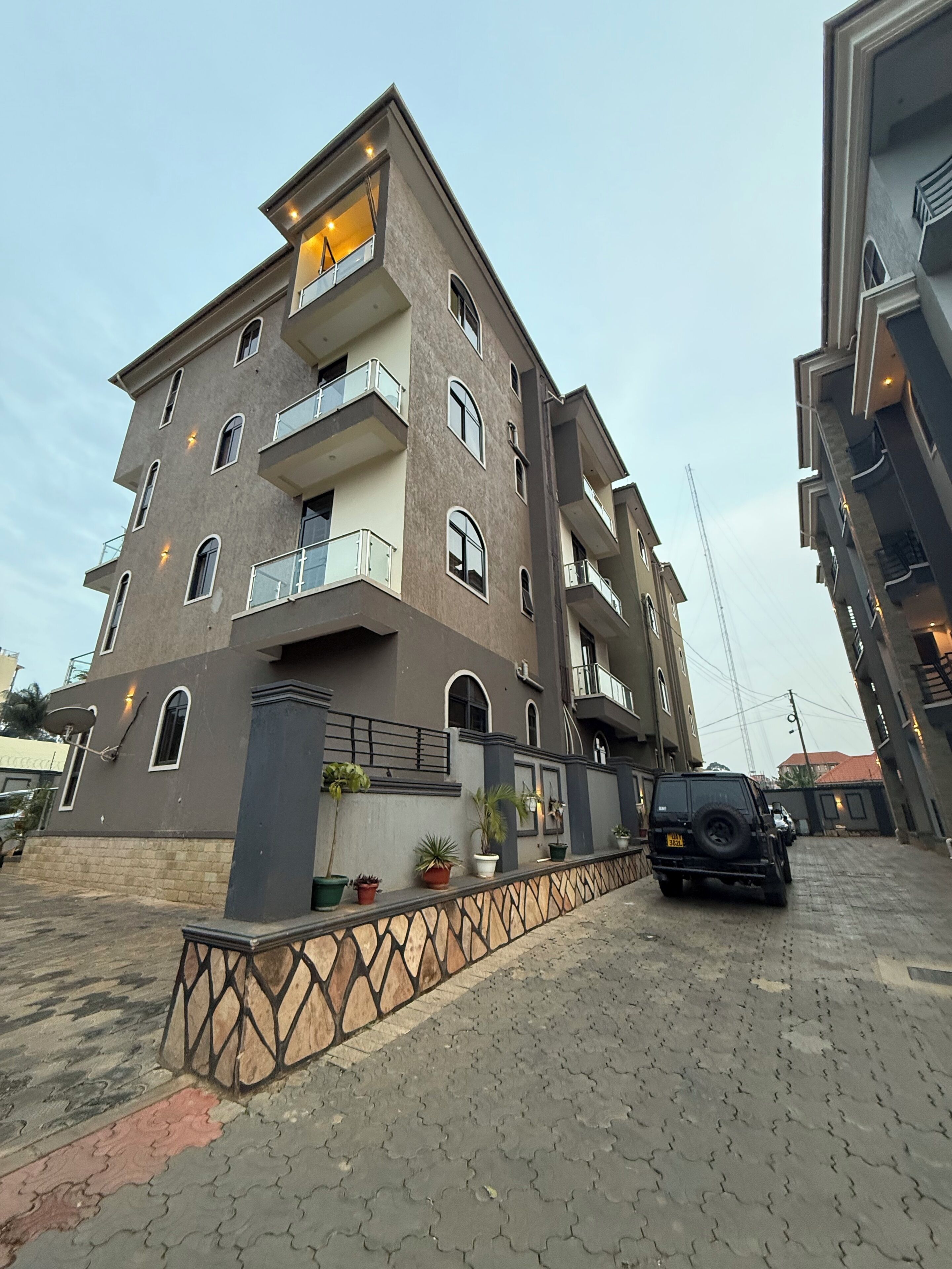 A multi-story residential building with balconies, potted plants, and a paved driveway.
