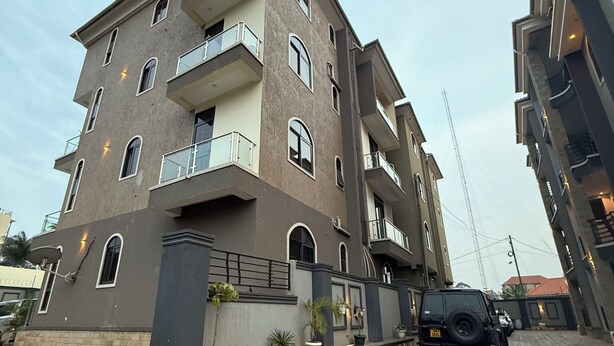 Un edificio residencial de varios pisos con balcones, plantas en macetas y un camino de entrada pavimentado.