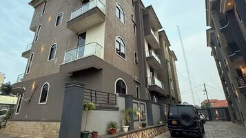A multi-story residential building with balconies, potted plants, and a paved driveway.