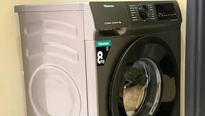 Lavadora Hisense de carga frontal con capacidad de 8 kg, ubicada en un rincón de una habitación con paredes amarillas y suelo de baldosas.