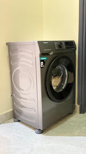 Een voorlader wasmachine van Hisense met een capaciteit van 8 kg, geplaatst in een hoek van een kamer met gele wanden en betegelde vloer.