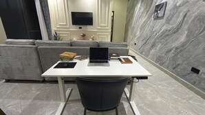 Una sala de estar moderna con un escritorio blanco, un sofá gris y un televisor montado en la pared.