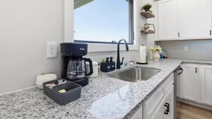 Una cocina con encimera de granito, cafetera, pileta y muebles blancos.