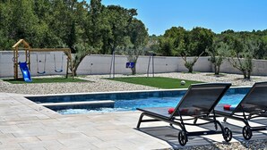 Un espace piscine comprenant des chaises longues, un toboggan et une aire de jeux clôturée.