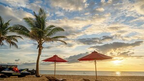 A beach with palm trees, red umbrellas, and lounge chairs. - Dolphin Beach Resort (Etalai)