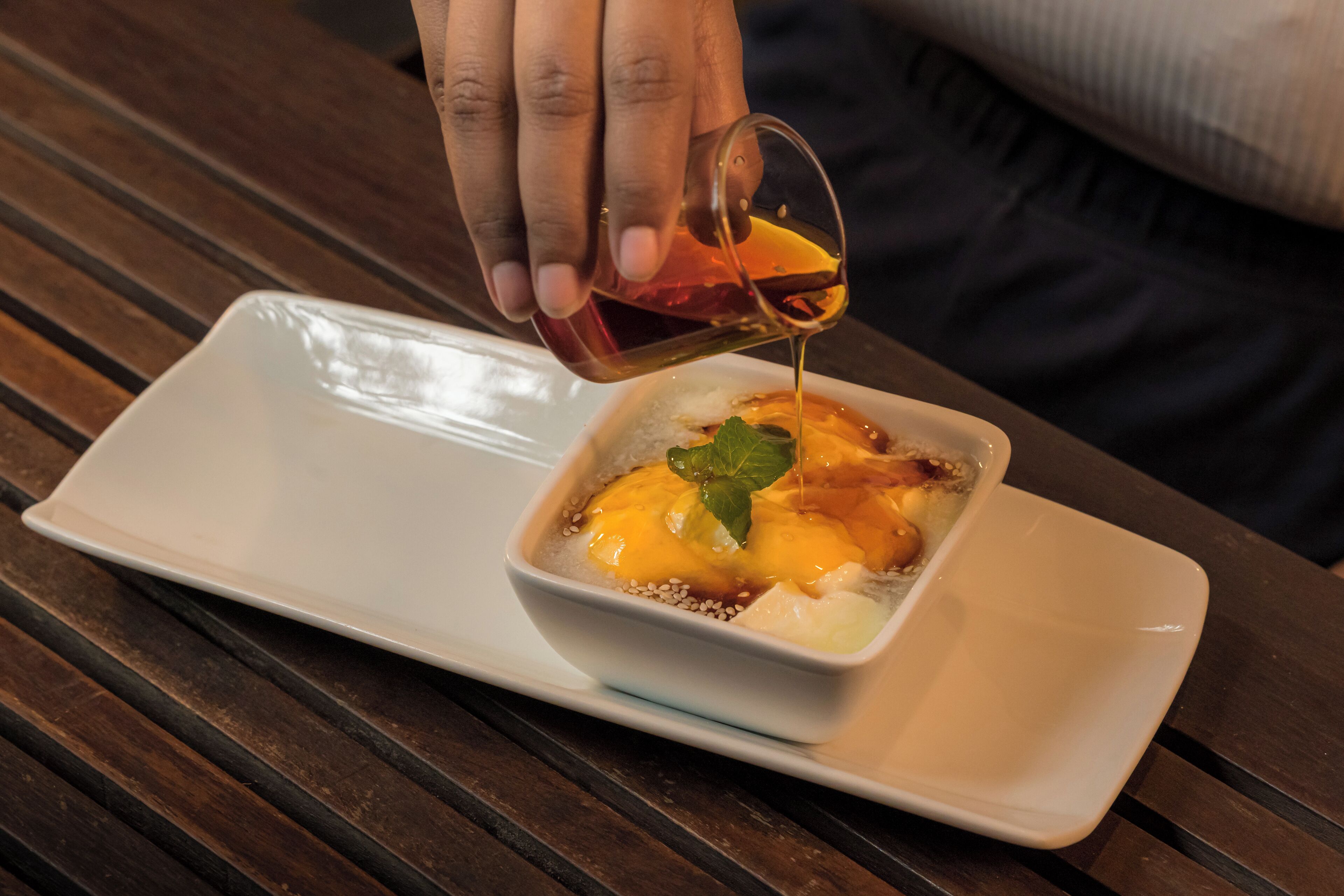 A hand pouring a sauce into a dish on a white plate.