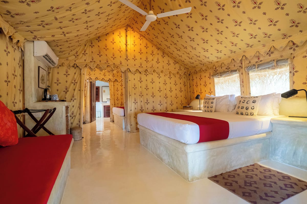 A room with a bed, a desk, and a chair. There is a ceiling fan, a window, and a door.