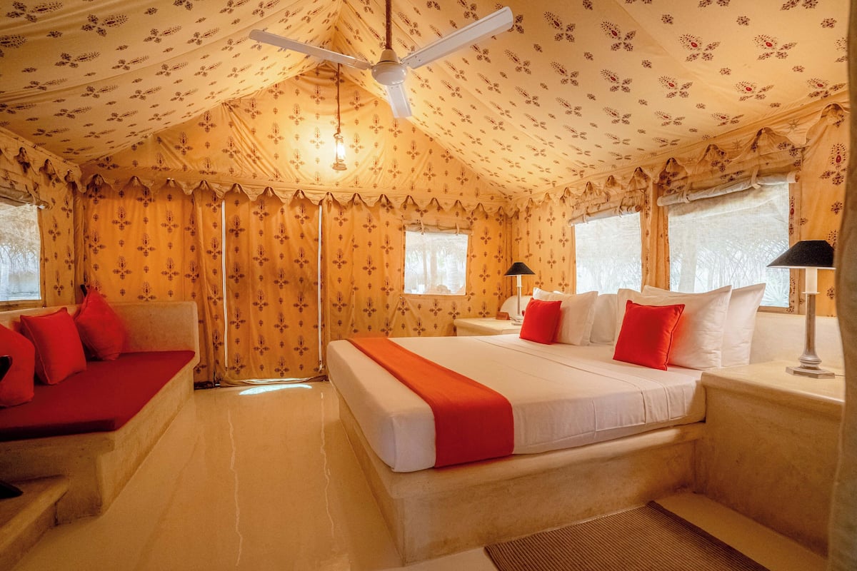 A room with a large bed, a sofa, a desk, and a ceiling fan.