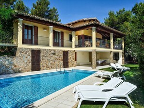 A two-story house with a swimming pool, stone walls, and a balcony with outdoor furniture. - Exclusive Villa with Pool and Sea View in Is Molas – Villa Le Poiane (S. Margh. di Pula)