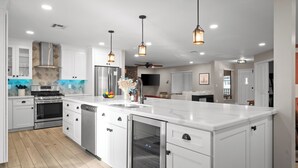 Une cuisine moderne avec des meubles blancs, des appareils en acier inoxydable et des luminaires suspendus.