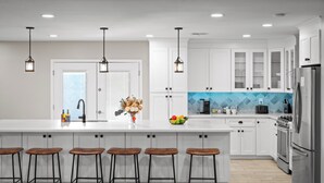 A modern kitchen with white cabinets, a large island with bar stools, stainless steel appliances, and pendant lighting. - Sleeps 16! Luxury Phoenix Retreat Near Biltmore- Pool, Theater & Game Room. (Phoenix)
