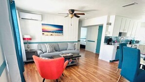 Un salon moderne avec un canapé, un fauteuil rouge et une table basse. On y trouve également un coin cuisine avec des meubles blancs et un fauteuil bleu.