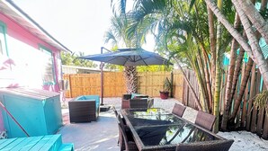 Une terrasse dotée d’une table à plateau de verre et de chaises en osier, entourée de palmiers et d’une clôture en bois.