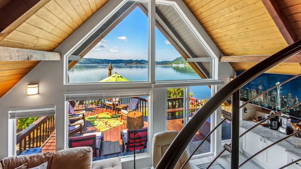 Une pièce spacieuse dotée d’une grande verrière, offrant une vue sur une terrasse aménagée avec du mobilier d’extérieur, et un escalier menant à un autre niveau.