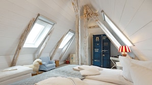 A cozy attic bedroom with a bed, a plush chair, a small table, and a wardrobe. - Spacious vacation home Lüttje Butt with garden and terrace near the beach on Sylt (List auf Sylt)