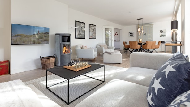 A modern living room with a fireplace, a dining area, and a kitchen in the background. - Spacious vacation home Lüttje Butt with garden and terrace near the beach on Sylt (List auf Sylt)